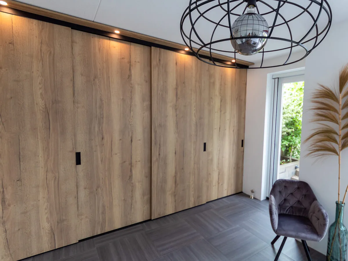 Wandbrede kastenwand in eikendecor met schuifdeuren en een verlichte bovenlijst in een woonkamer